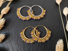 three pairs of beaded hoop earrings sitting on top of a table next to dried flowers