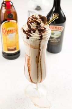 an ice cream sundae with chocolate sauce and whipped cream in a glass next to bottles