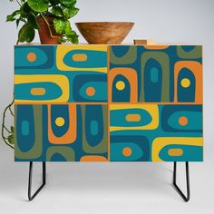 a potted plant sitting on top of a blue and yellow cabinet with an abstract design