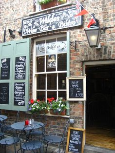 the outside of a restaurant with tables, chairs and chalkboard menus on the wall