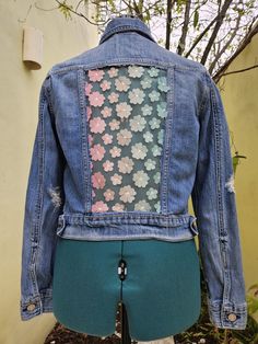 the back of a jean jacket with flowers on it, sitting on top of a mannequin