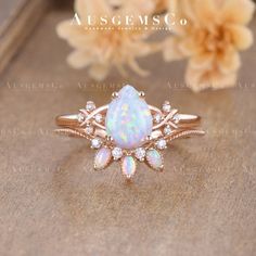 an opal and diamond ring sits on top of a wooden table next to flowers