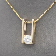 This brilliant sparkler is beautifully crafted and emanates richness. The pendant is rectangular and holds a round brilliant cut natural diamond at the base in a tension setting. The integral bail is large enough to accommodate a large chain or small omega, measuring about 6mm in width at the widest area. The pendant hangs on a thicker-than-normal box chain necklace with features a spring ring clasp. The result is a stunning simplicity, looking equally elegant in casual and dress ensembles. The Modern Diamond Solitaire Necklace, Diamond Necklace Men, 3 Stone Pendant, Mens Ring Designs, Pendant Ideas, Tension Setting, Jewelry Designing, Diamond Rings Design, Diamond Solitaire Necklace