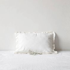 a white pillow on top of a bed next to a wall with a plant in it