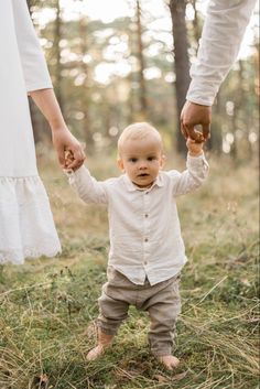 a little boy holding the hand of his mother's hand in a forest setting