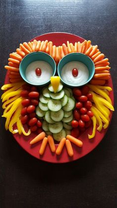 an owl made out of fruits and vegetables on a red plate with two bowls in the shape of eyes