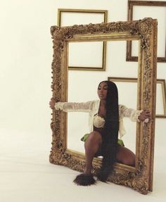 a woman sitting in front of a mirror with her legs crossed and hands on the frame