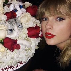 a woman holding a cake decorated with white flowers and a cat on it's face