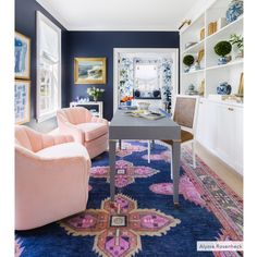 a living room with blue walls and pink chairs