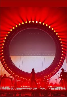 a woman standing in front of a giant mirror on stage with lights around her and people watching