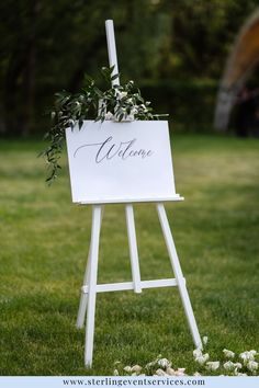 a welcome sign with greenery on it in the grass at an outdoor wedding ceremony