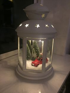 a white lantern sitting on top of a counter filled with snow and christmas trees in it