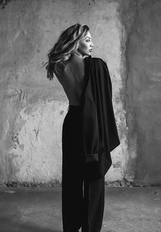 black and white photograph of a woman with her back to the camera, standing in front of a wall