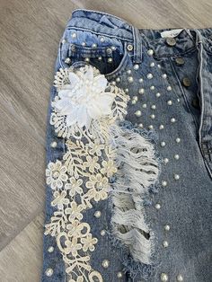 an old pair of jeans with embroidered flowers and pearls on the side, sitting on a wooden floor