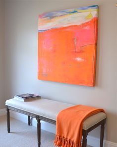 a painting hangs on the wall above a bench with an orange blanket draped over it