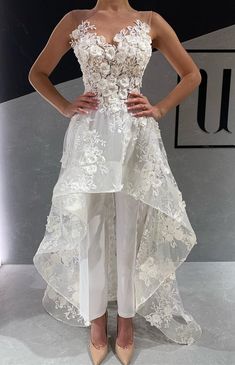 a woman standing on top of a runway wearing white pants and a dress with flowers