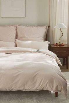 a bed with pink sheets and pillows in a bedroom next to a lamp on a table