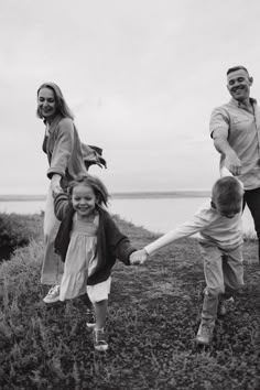 a man and two children are holding hands as they run across the grass near water