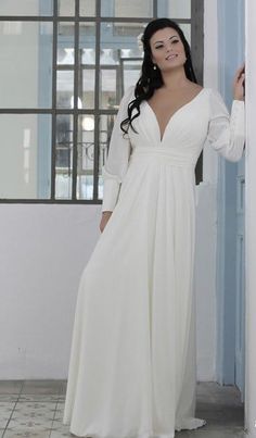 a woman in a long white dress leaning against a wall with her hands on her hips