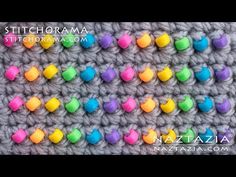 colorful crochet stitchs are arranged on the side of a gray blanket with multicolored hearts