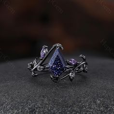 a ring with purple stones and leaves on it, sitting on top of a rock