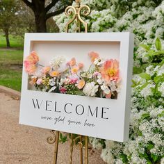 a welcome sign with flowers on it sitting in front of some white and pink flowers