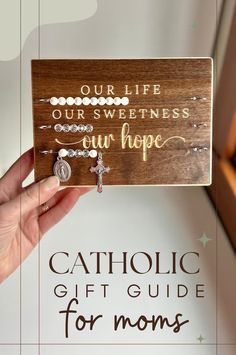 a hand holding up a wooden sign that says our life our sweetness our hope catholic gift guide for moms