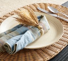 a plate with two napkins on it next to a fork and spoon sitting on a woven place mat