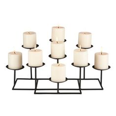 twelve white candles are arranged on a black metal stand, with one candle lit in the middle