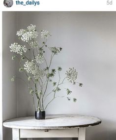 some white flowers are in a black vase on a marble top table next to a gray wall