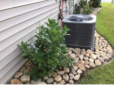 an air conditioner sitting on the side of a house next to a flower bed