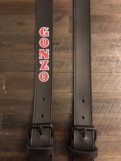 two black leather belts with the word gonzo on them sitting on top of a wooden floor