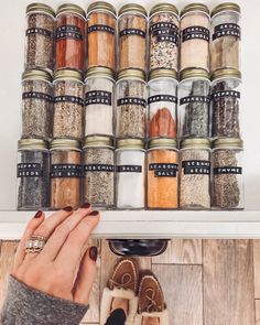 someone holding their hand up to a shelf full of spice jars and spices on it