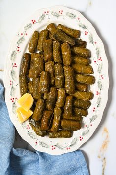 a white plate topped with stuffed grape leaves next to a slice of lemon wedges