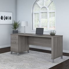 an office desk with a laptop on it in front of a large window and rug