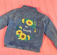 a denim jacket with sunflowers and the words merry country on it, sitting on a pink surface