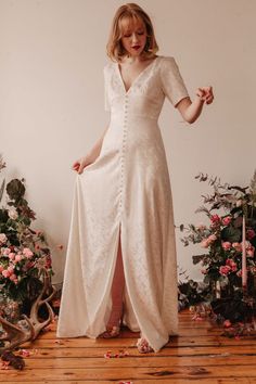 a woman in a white dress is standing on a wooden floor with flowers around her