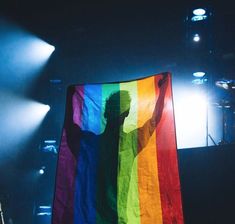 a person holding a rainbow flag in front of a stage with spotlights on it