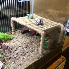 there is a small table made out of rope and rocks in an aquarium tank with plants on the side