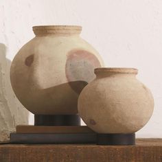 two vases sitting on top of a wooden table next to each other in front of a white wall