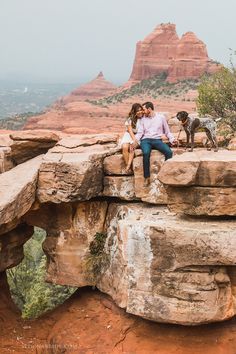 a man and woman sitting on top of a rock formation with two dogs looking at each other