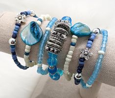 Combine and save on these gorgeous bracelets for a dazzling stack of SEVEN bracelets at over a 25% discount! 1. Silver flower bracelet: These sweet bracelets are made with various shades of blue glass beads and silver flower and round beaded accents  2. Blue shell bracelet: A blue shell centerpiece flanked by white glass beads 3. White and blue bracelet: Blue and white glass beads create the perfect accessory to support any statement piece 4. Chunky blue glass bracelet: Shades of blue glass with Blue Stackable Bracelets For Summer, Blue Stackable Wrap Bracelet As Gift, Adjustable Blue Stackable Wrap Bracelet, Blue Stackable Jewelry For Summer, Blue Bracelets With Unique Round Beads, Blue Bracelets With Unique Variations, Blue Beaded Bracelets With Extender, White And Blue Bracelet, Shell Centerpieces