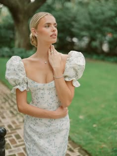 a woman in a white dress is posing for the camera with her hand on her face