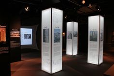 three tall white displays in a dark room with lights on the ceiling and pictures on the walls