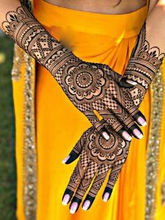 a woman with henna on her hands and yellow dress in front of some grass