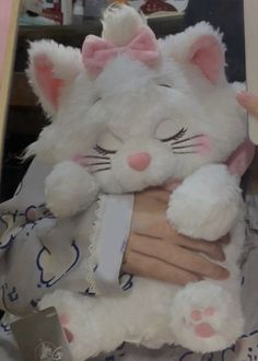 a person holding a white stuffed cat in their arms and wearing a pink bow on her head