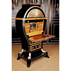 an old fashioned black and gold desk with fan on it's top, sitting in front of a wall