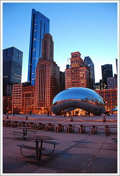 the city skyline is lit up at night, with benches and tables in front of it