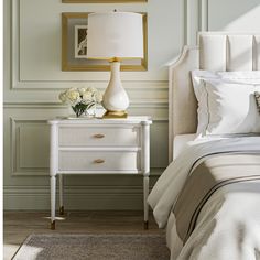 a white nightstand with flowers on it next to a bed