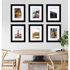 four black and white framed pictures hang on the wall above a wooden table with two chairs